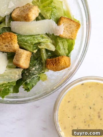 bowl of salad next to a small bowl of caesar dressing.