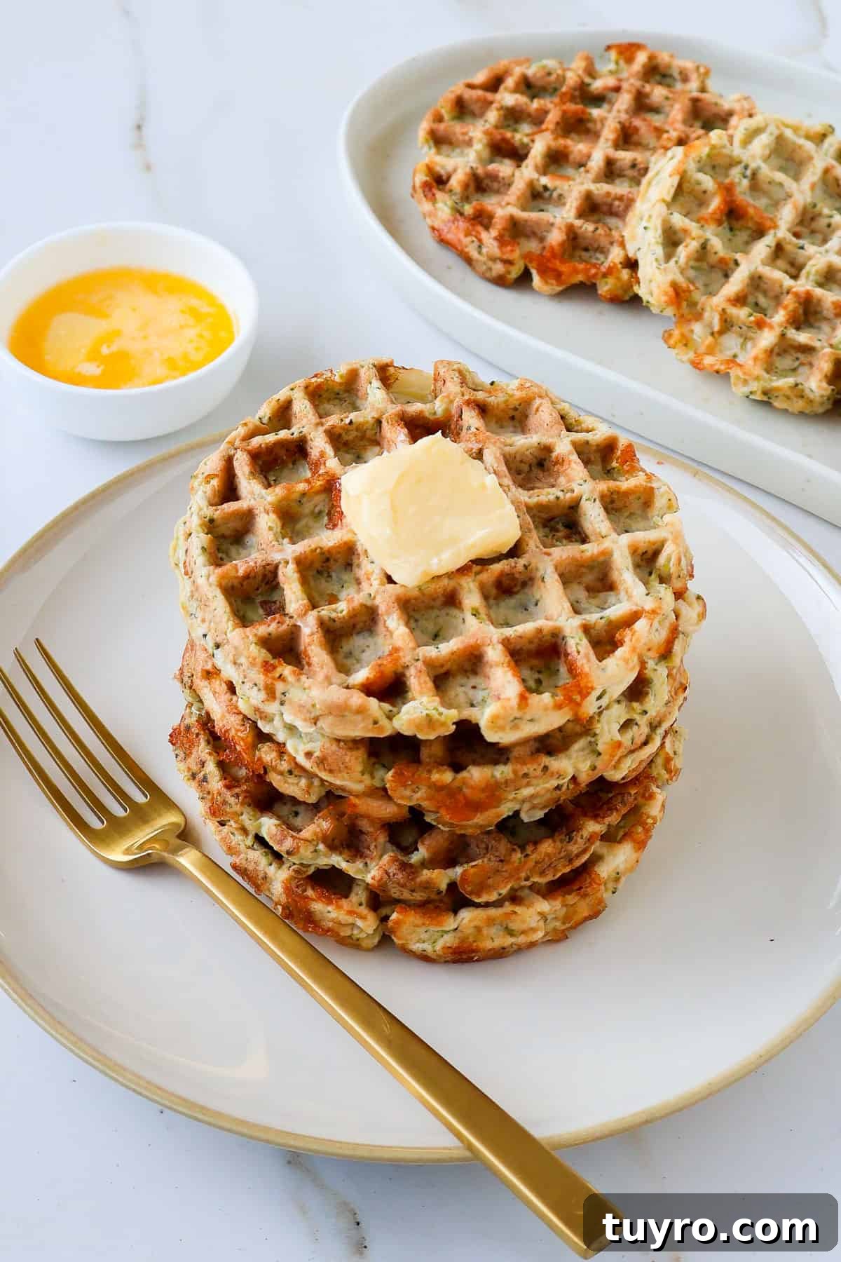 Broccoli Cheddar Waffles Recipe 3 Side shot of broccoli waffles stacked on a plate topped with a knob of butter.