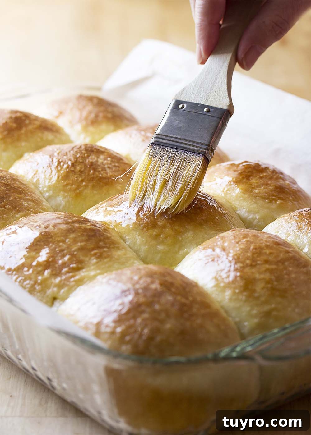 A pan of rolls hot from the oven being brushed with melted butter.