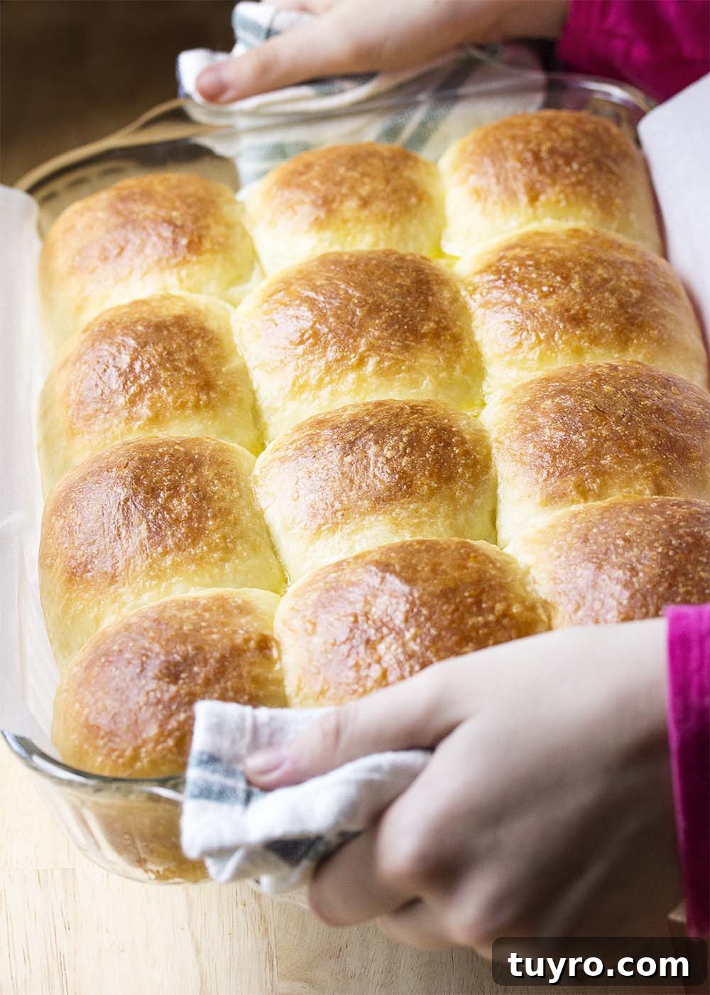 Hands holding up the baking pan of finished golden brown and buttery rolls.