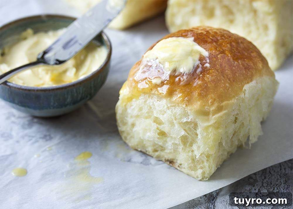 A soft and fluffy dinner roll covered in butter and ready to eat.