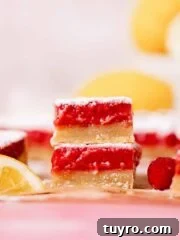 two lemon raspberry squares stacked on top of each other with tangy raspberry filling and shortbread crust