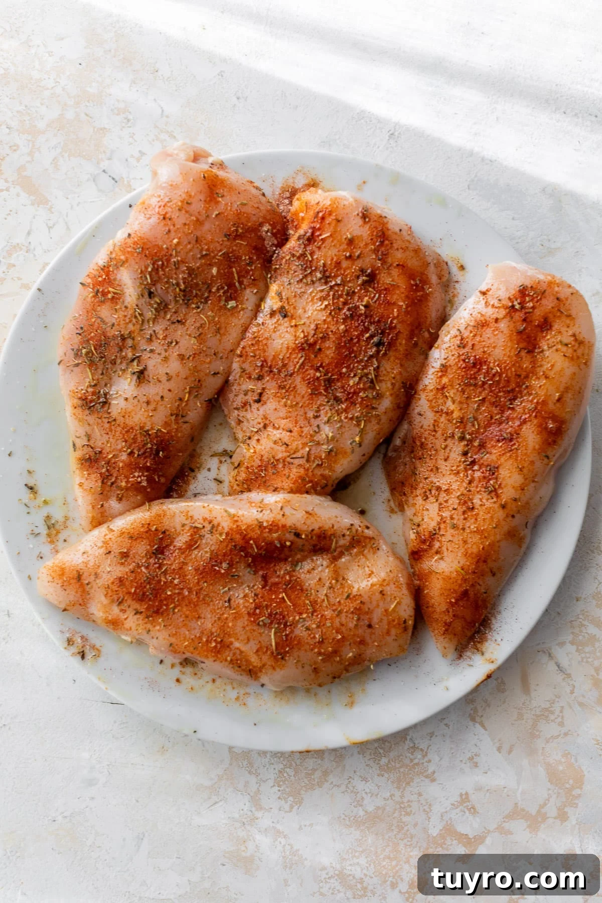 Tender Slow-Cooker Chicken Breast Recipe for Quick Meals 4 4 raw seasoned chicken breasts on a white plate.