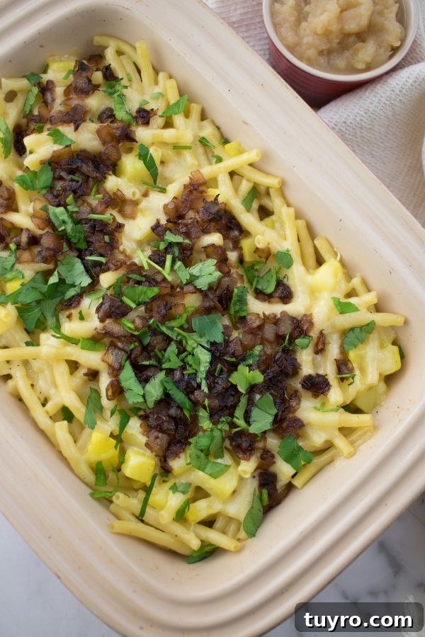 layers of macaroni, cheese, potatoes, onions and parsley in a red baking dish with applesauce on the side