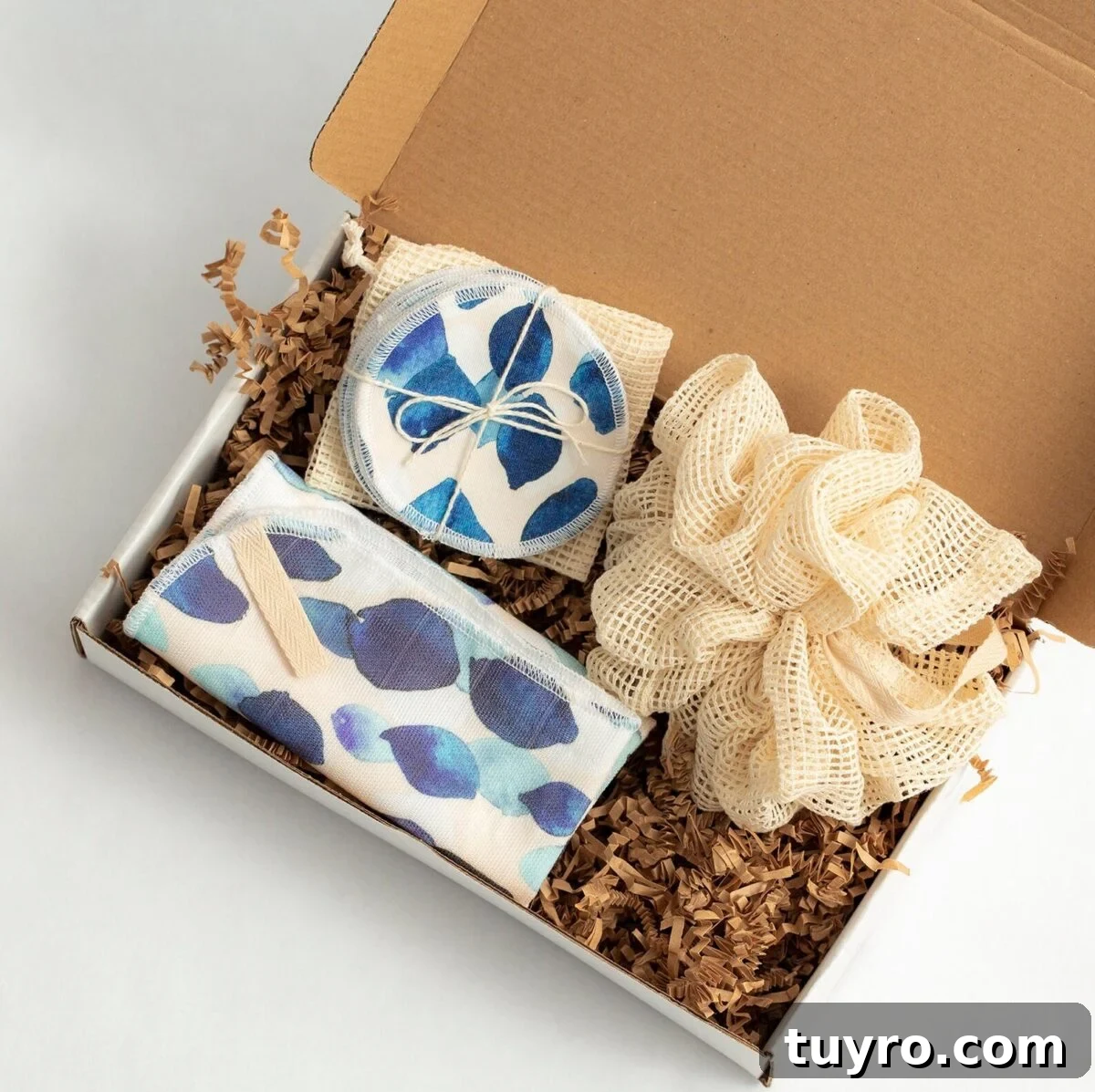 Eco-friendly gift box containing reusable makeup remover pads with blue leaf pattern and mesh produce bag nestled in kraft paper shred