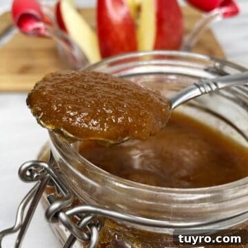 A teaspoon with apple juice reduction over a glass jar with apples in the background.