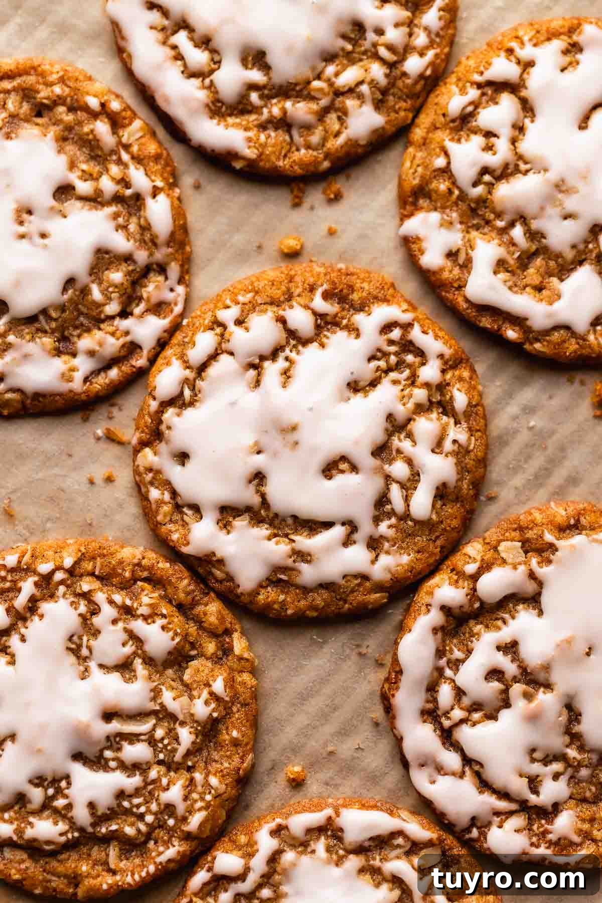 Soft Iced Oatmeal Cookies Recipe with Chewy Texture and Vanilla Glaze 2 Iced oatmeal cookies on a brown parchment paper lined baking tray.