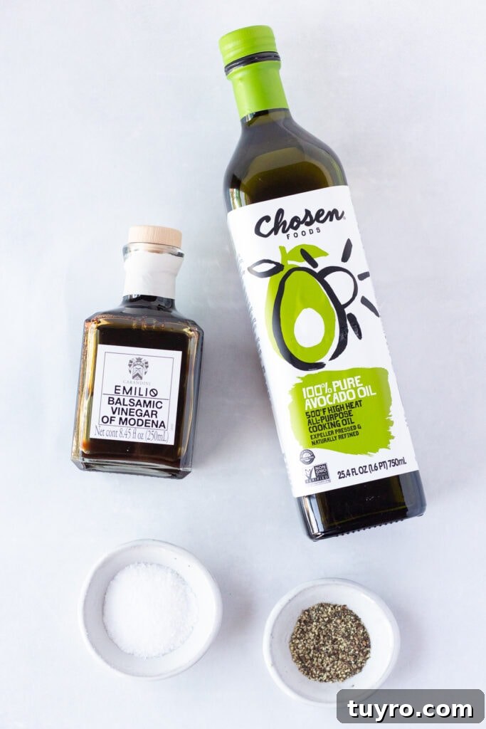 Top down shot of a bottle of avocado oil, a bottle of balsamic vinegar, and two small bowls with salt and pepper in them, respectively, all on a white background.