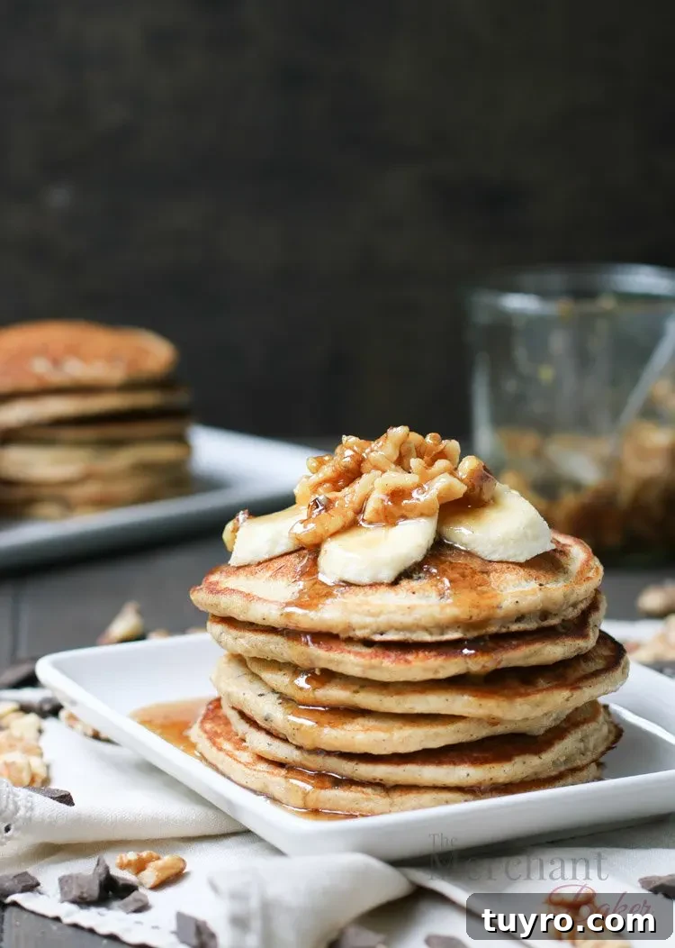 Stack of Oatmeal Chocolate Chip Banana Pancakes topped with sliced bananas and walnut syrup