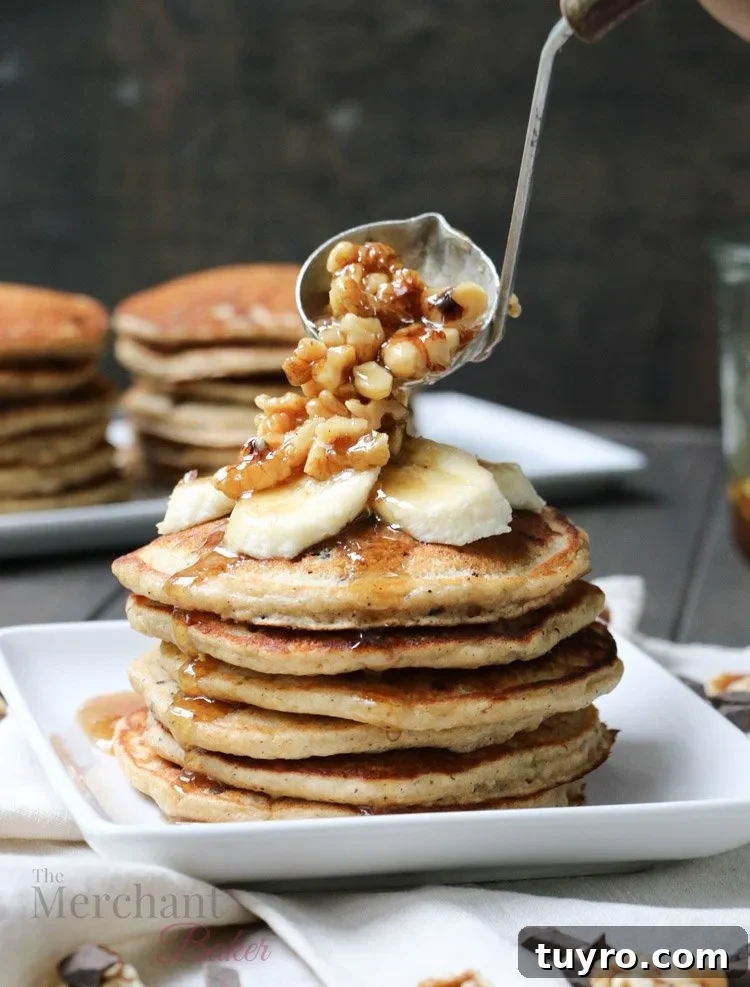Walnut syrup being ladled over a stack of Oatmeal Chocolate Chip Banana Pancakes topped with sliced bananas