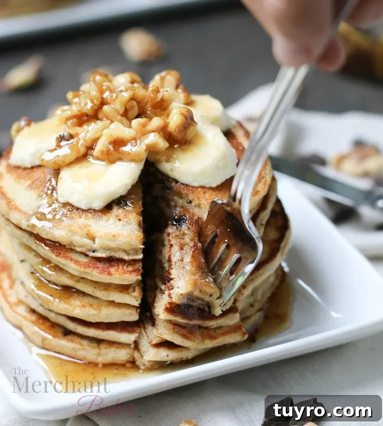 Stack of Oatmeal Chocolate Chip Banana Pancakes speared with a fork topped with sliced bananas and walnut syrup