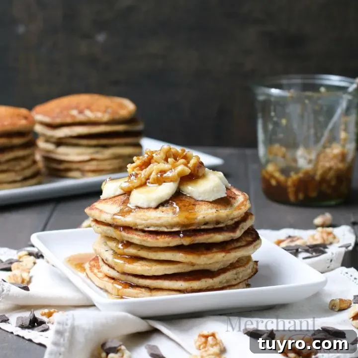 Stack of Oatmeal Chocolate Chip Banana Pancakes topped with sliced bananas and walnut syrup from themerchantbaker.com