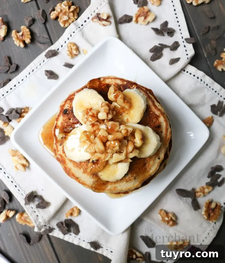 Overhead view of Stack of Oatmeal Chocolate Chip Banana Pancakes topped with sliced bananas and walnut syrup
