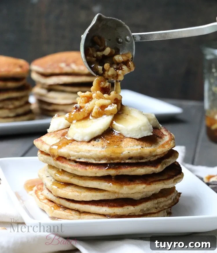 Walnut syrup being ladled over a stack of Oatmeal Chocolate Chip Banana Pancakes topped with sliced bananas