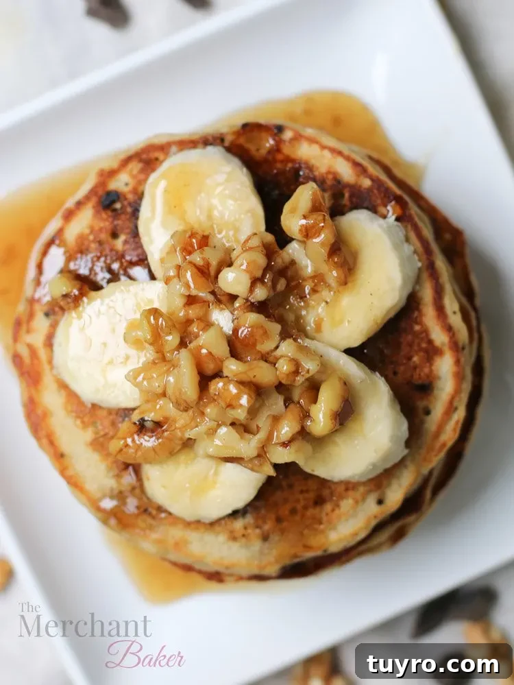 Overhead view of Stack of Oatmeal Chocolate Chip Banana Pancakes topped with sliced bananas and walnut syrup