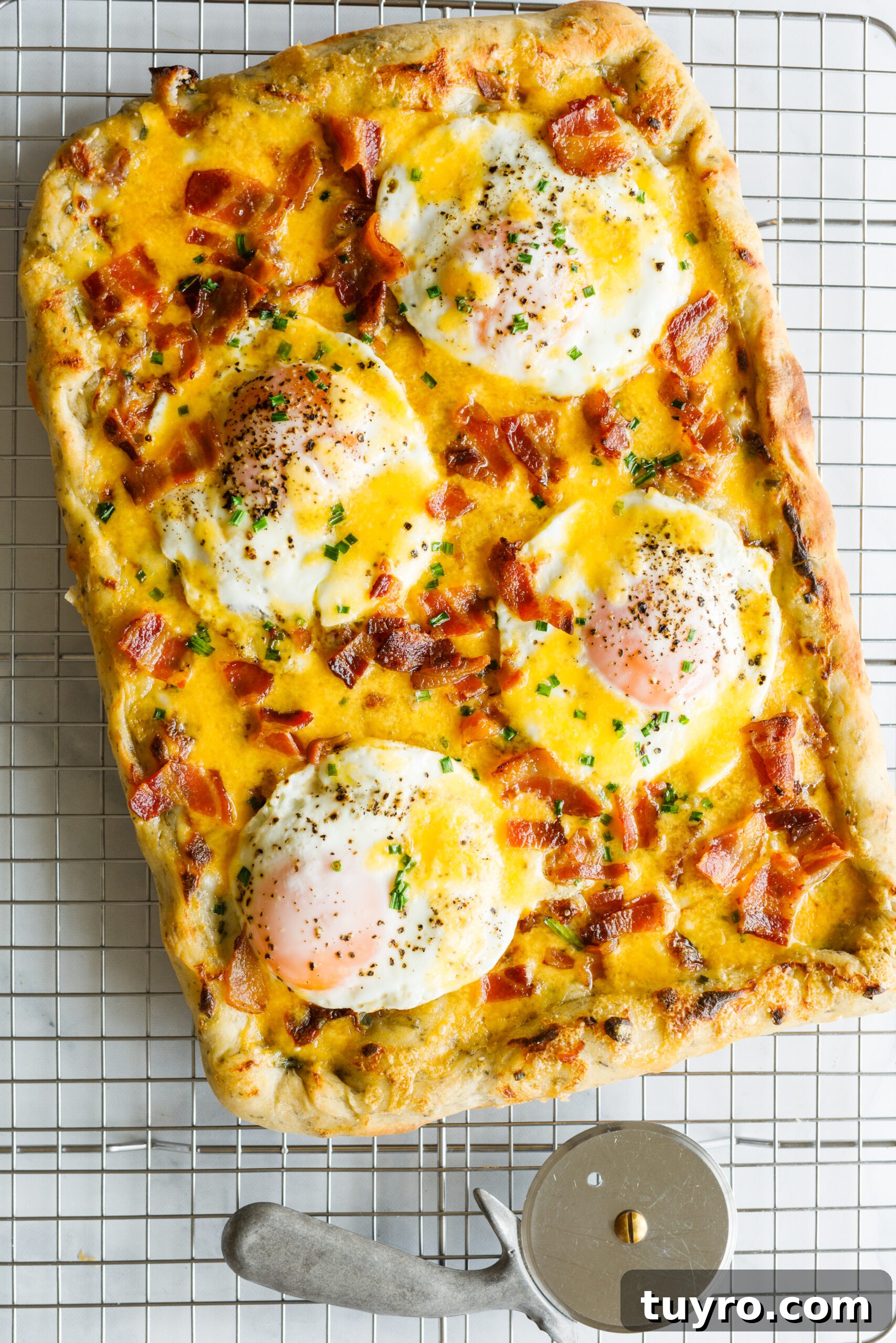 The Easy Bacon and Egg Pizza on a cooling rack with a pizza cutter