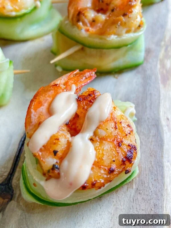 A grilled shrimp topped with creamy sauce rests on a cucumber boat, secured with a toothpick, and served on a wooden surface.