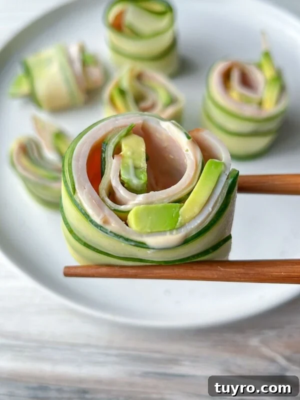 Chopsticks hold a Cucumber and Avocado Roll made with ham, while more cucumber and avocado rolls are arranged on a white plate in the background.