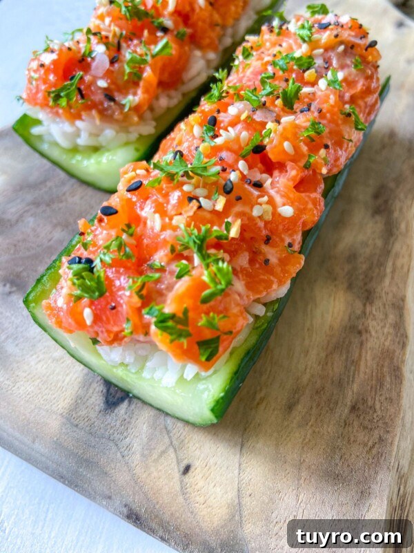 Enjoy Cucumber Salmon Boats—two cucumber boats filled with white rice and topped with diced salmon, sprinkled with black and white sesame seeds and chopped parsley, served on a wooden board.