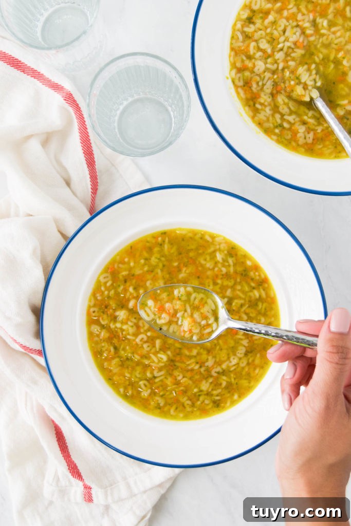 Classic Alphabet Soup Recipe with Homemade Broth and Tender Pasta 6 A woman holds a spoon above a bowl of Alphabet Soup