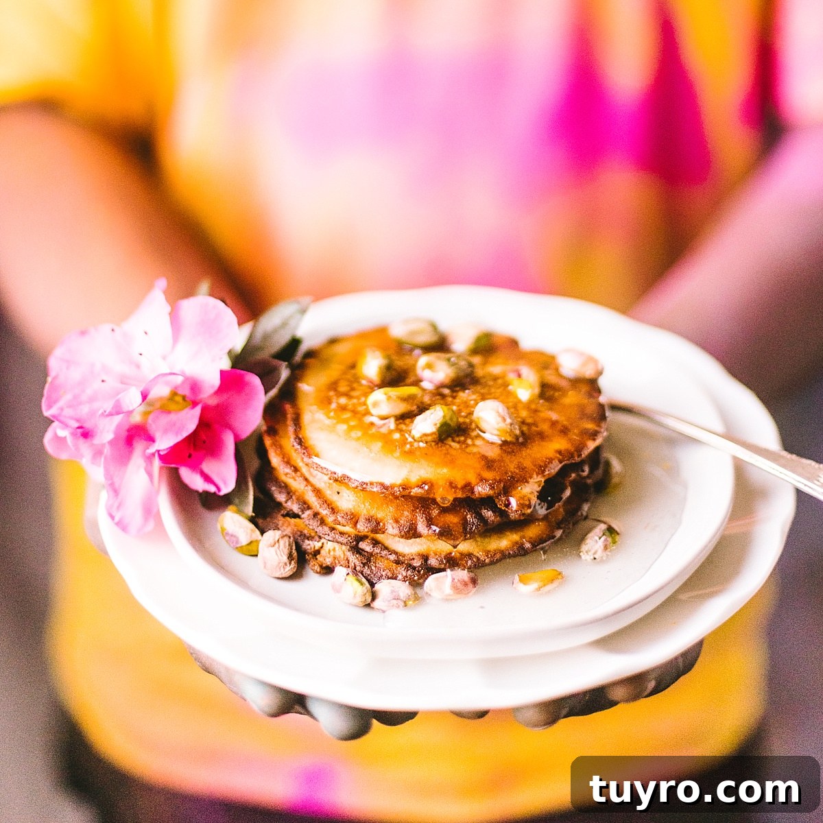 hands covered with holi powder holds bengali malpua dripping with syrup and covered with pistachios