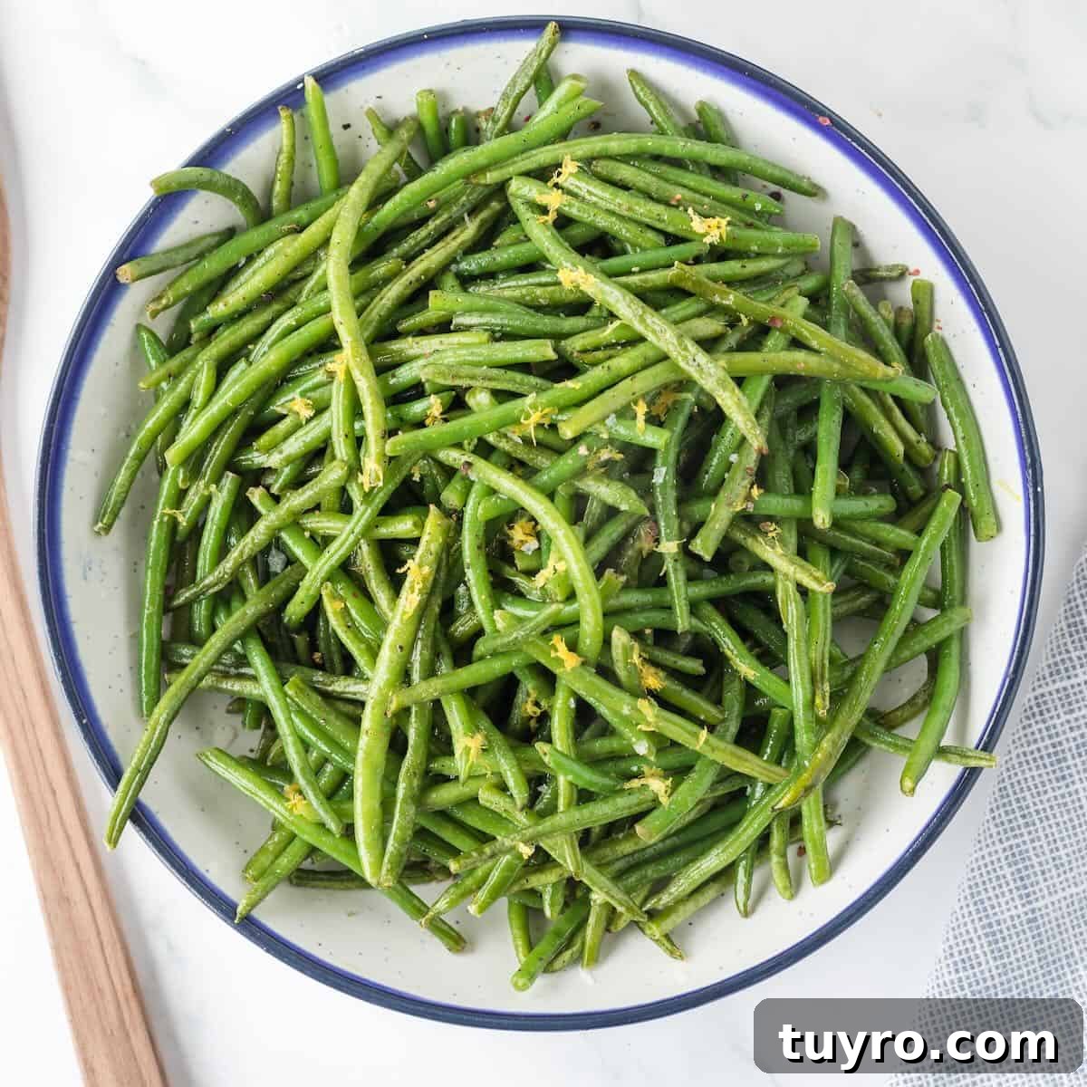 A bowl of cooked green beans fresh from the air fryer, garnished with lemon zest.
