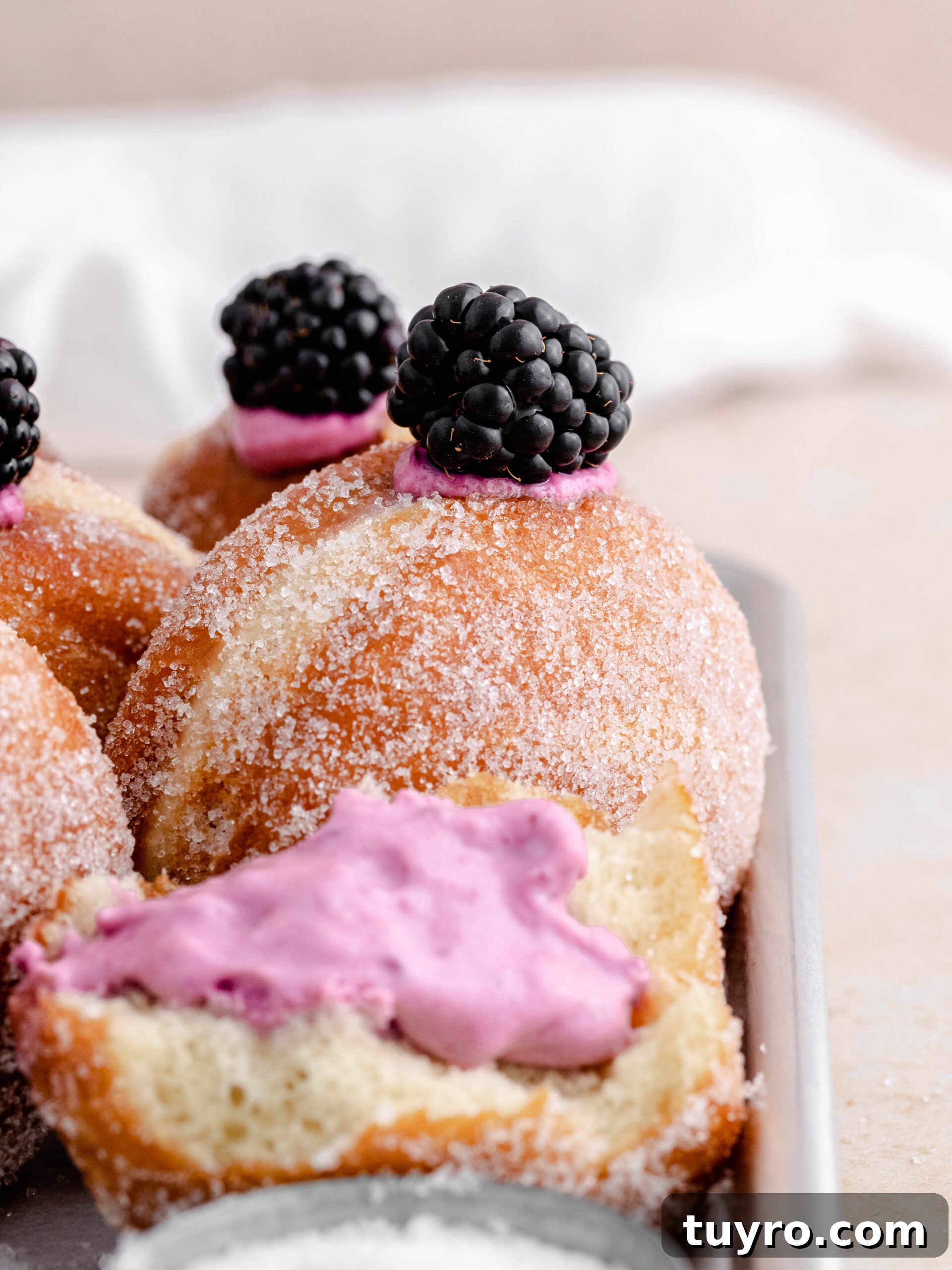 Blackberry Cheesecake Donuts with Creamy Filling 6 Filled blackberry cheesecake donuts on a tray.