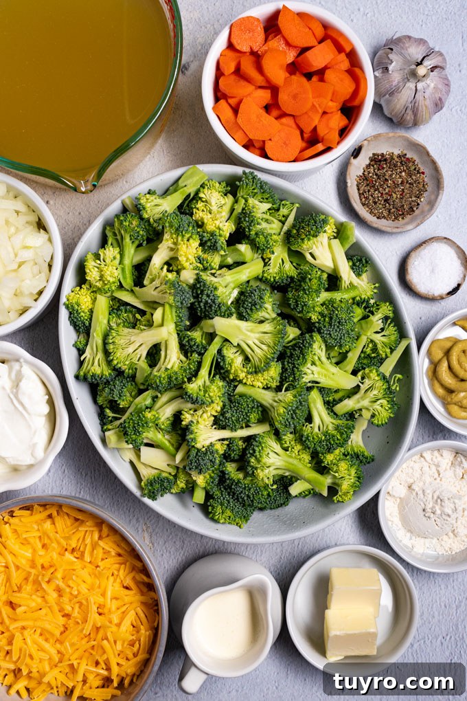 Creamy Broccoli Cheddar Soup Recipe with Gluten-Free Option 3 Overhead photo of ingredients in bowls: broccoli florets, shredded cheddar cheese, chopped onion, sliced carrots, garlic cloves, chicken broth, cream, butter, and flour.