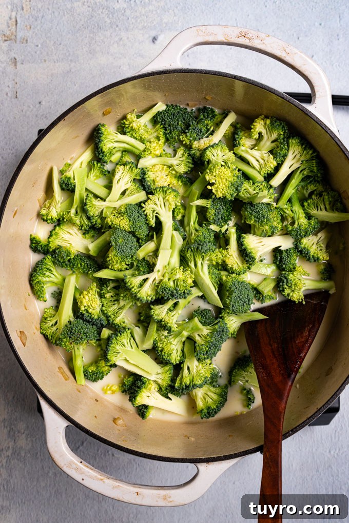 Creamy Broccoli Cheddar Soup Recipe with Gluten-Free Option 5 Overhead shot of broccoli florets in a white Dutch oven with soup base underneath. A wooden spoon is resting in the Dutch oven. #foodphotography