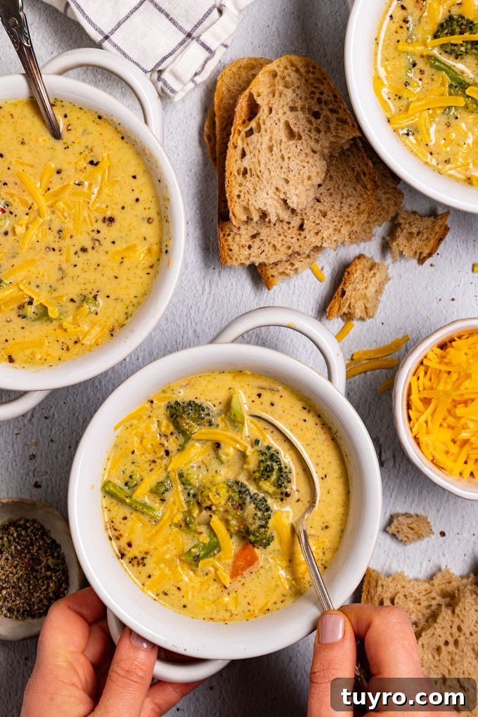 Creamy Broccoli Cheddar Soup Recipe with Gluten-Free Option 7 Overhead photo of healthy broccoli cheddar soup in a white bowl. A hand is holding a spoonful of the soup. There is a bowl of soup in the upper left corner as well, and another bowl of soup in the upper right corner. Slices of bread are scattered through the scene. #foodphtoography