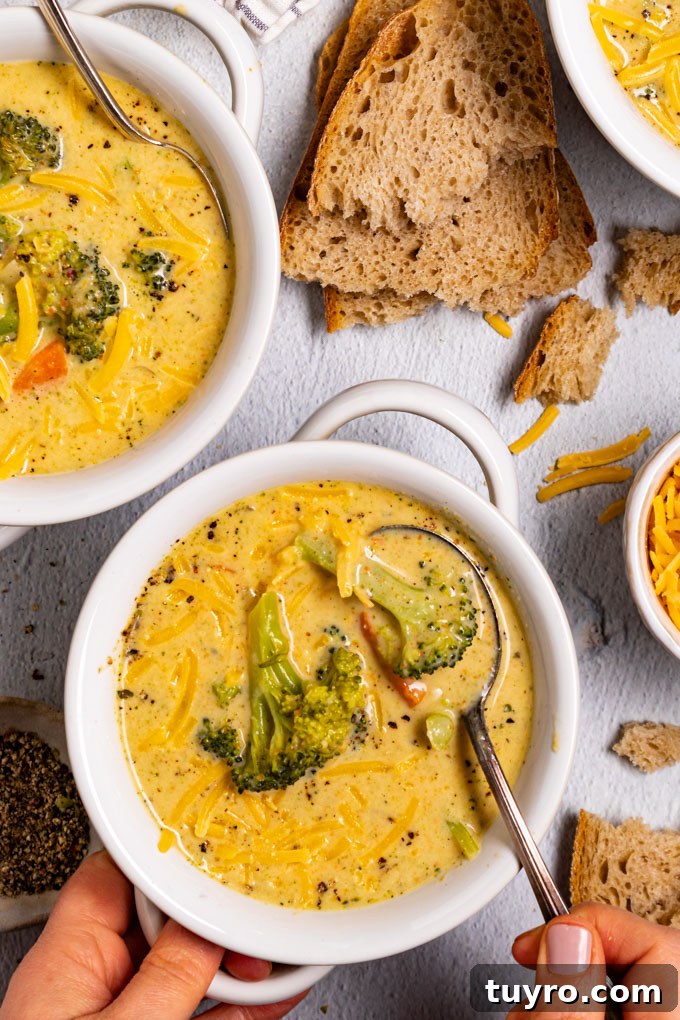 Creamy Broccoli Cheddar Soup Recipe with Gluten-Free Option 8 Close up overhead photo of healthy broccoli cheddar soup in a white bowl. A hand is holding a spoonful of the soup. There is a bowl of soup in the upper left corner, and another bowl of soup in the upper right corner. #foodphtoography