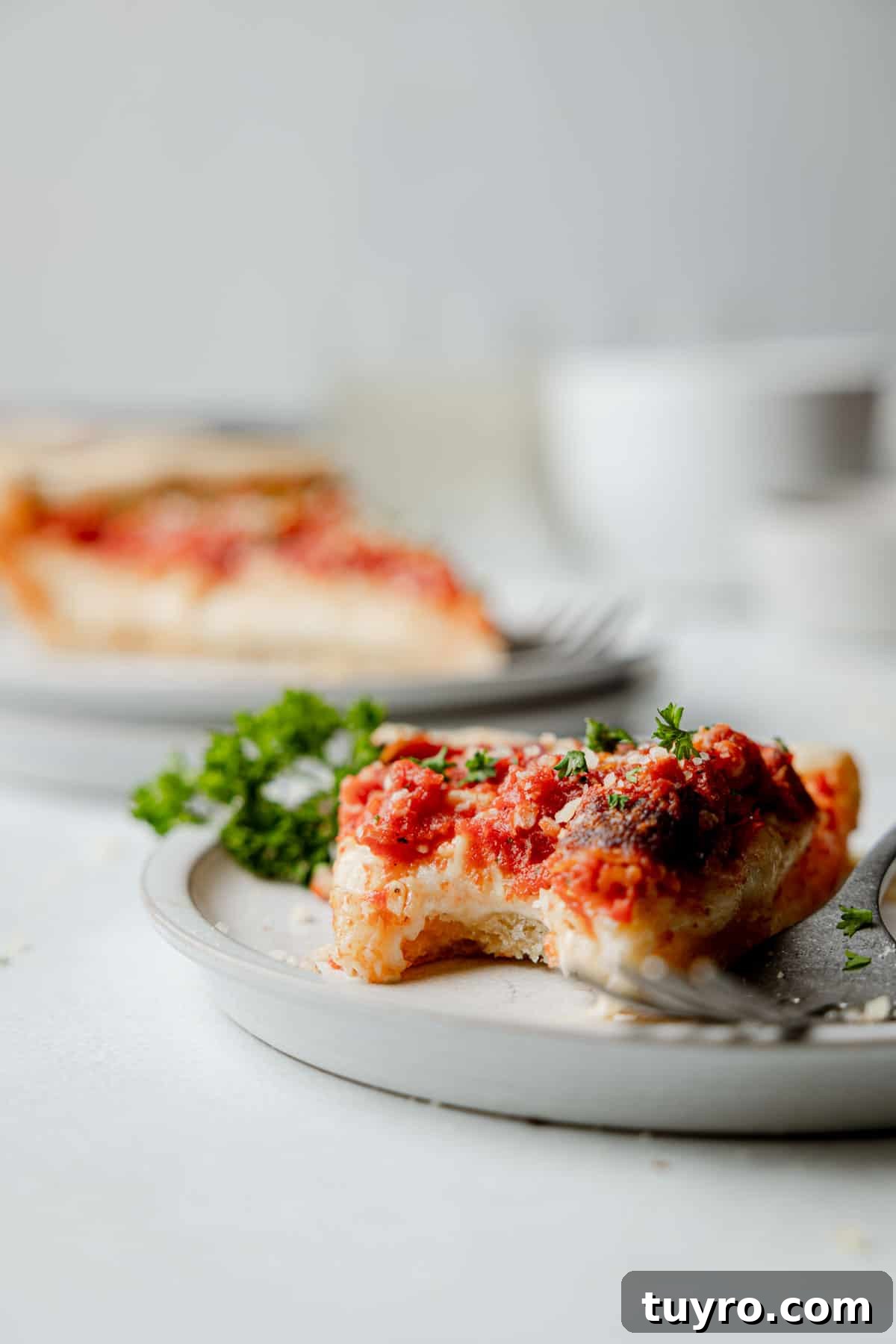 Authentic Chicago-Style Gluten-Free Deep Dish Pizza Recipe 13 A slice of gluten free deep dish pizza on a small plate with bite taken, garnished with parsley.