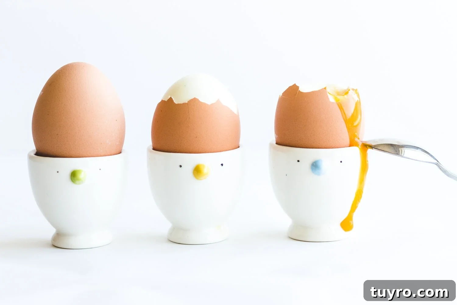 How to Make Creamy Soft-Boiled Eggs Every Time 6 Three soft boiled eggs in egg cups with yolk running down the side of the last one and a spoon resting against it