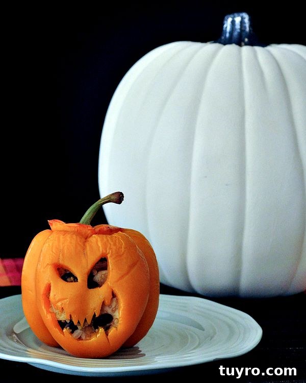 Chipotle Tofu Stuffed Peppers @spabettie Chipotle coconut tofu filling stuffed into an orange bell pepper carved like a jack o lantern, on a green plate next to a white pumpkin.