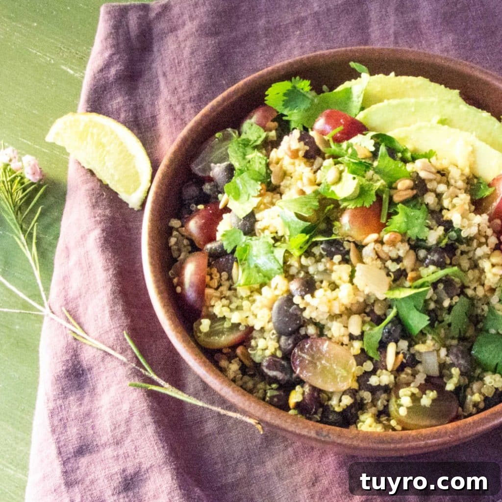 A bowl of quinoa, black beans, grapes, avocado and cilantro, on a tea towel with a slice of lime.