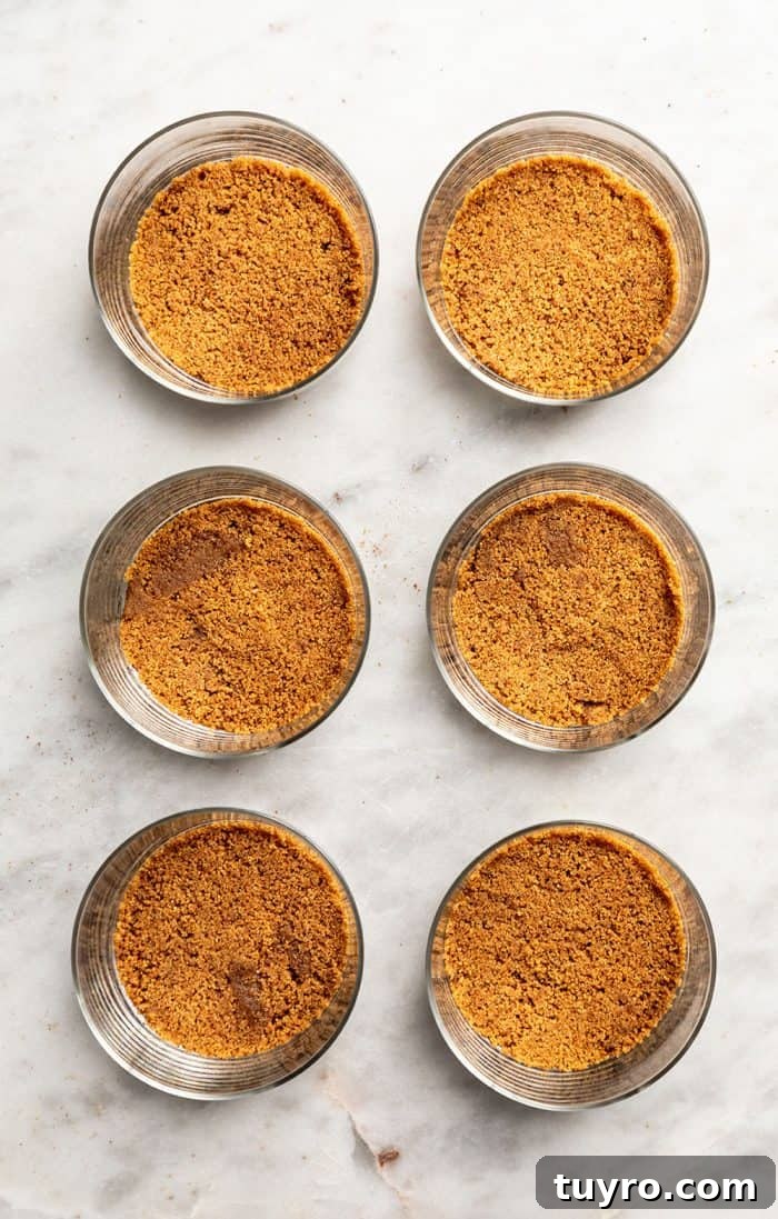 Mini No-Bake Cranberry Cheesecakes with Gingersnap Crust 7 Gingersnap cookie crusts in the bottom of six glass containers lined up on a marble countertop