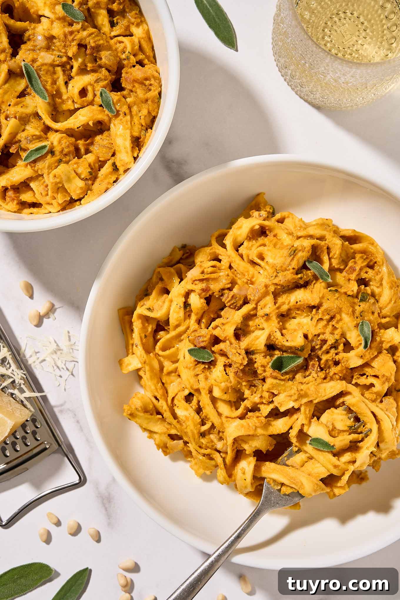 Creamy Pumpkin Pasta with Crispy Pancetta and Parmesan 2 Two bowls of creamy pumpkin pasta with pancetta and sage served in white bowls, a glass of white wine and cheese grater in the background.