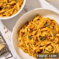 Creamy Pumpkin Pasta with Crispy Pancetta and Parmesan 9 Two bowls of creamy pumpkin pasta with pancetta and sage served in white bowls, a glass of white wine and cheese grater in the background.