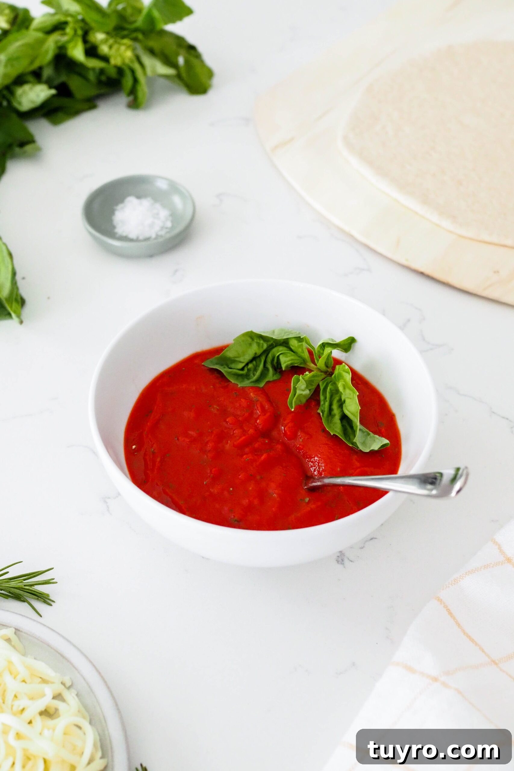 How to Make Pizza Sauce with Tomato Paste 2 A bowl of pizza sauce next to a bunch of basil and a rolled out pizza crust.
