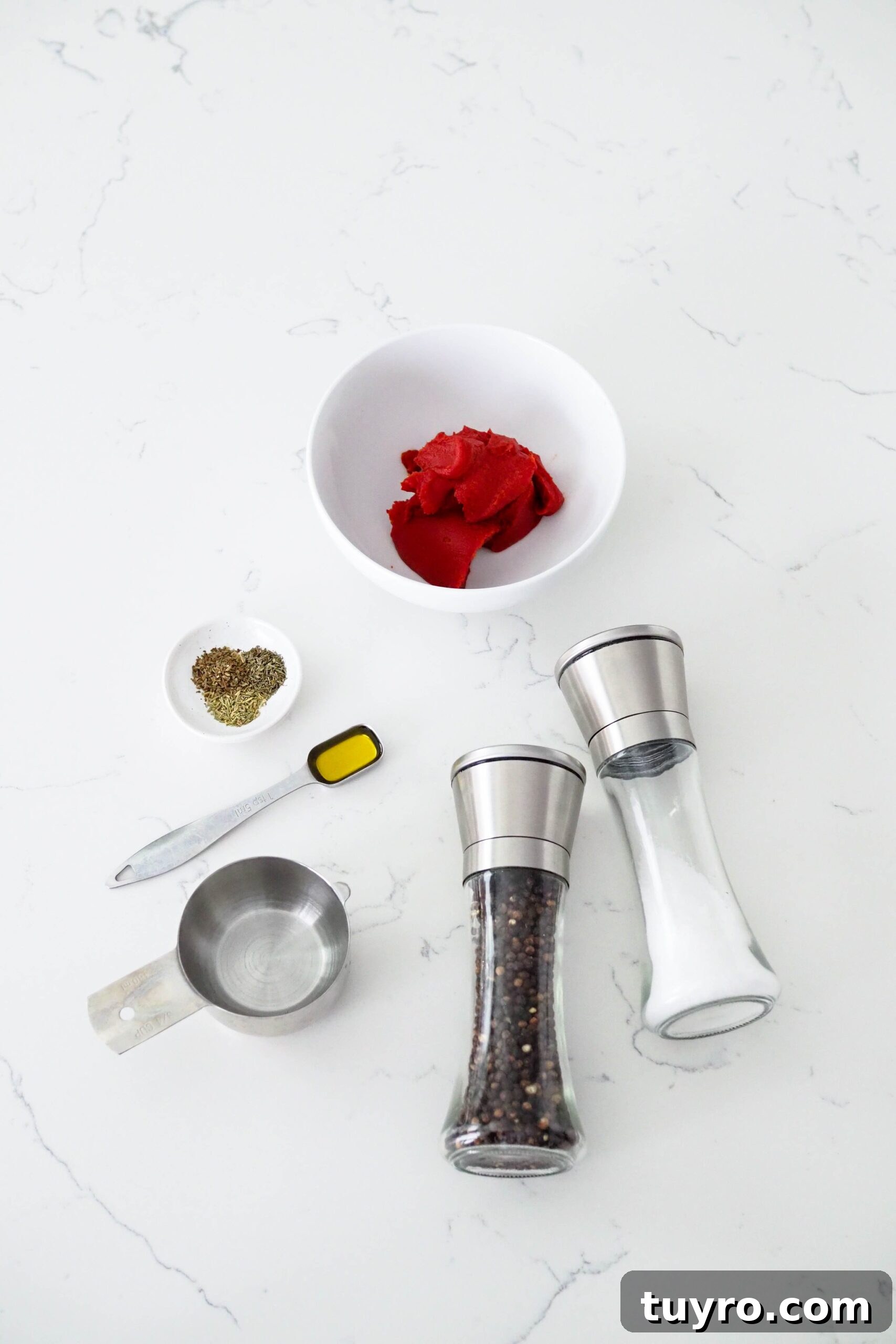 How to Make Pizza Sauce with Tomato Paste 3 Tomato paste, salt and pepper, water, olive oil, and spices on a white counter.