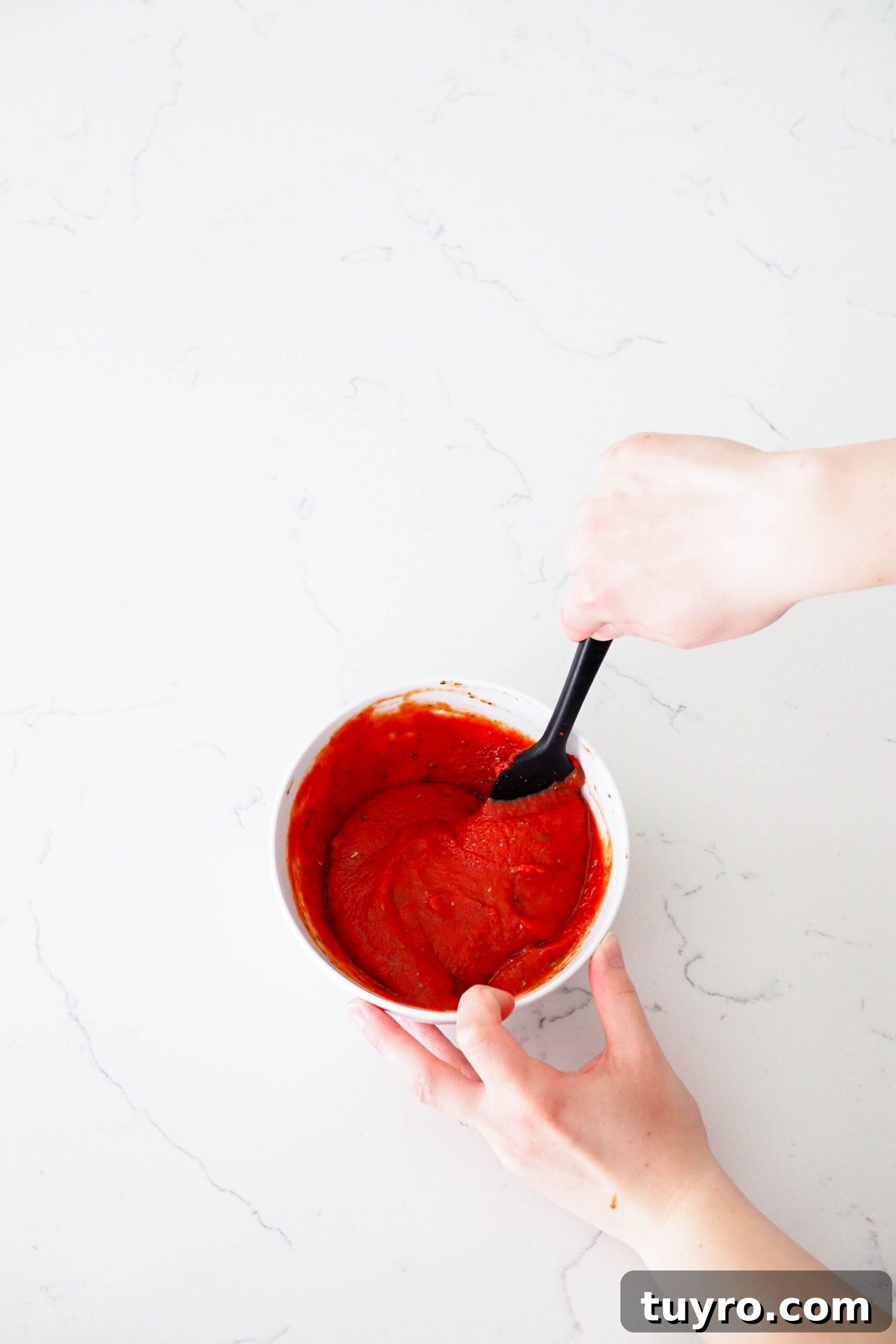 How to Make Pizza Sauce with Tomato Paste 5 A hand stirs together pizza sauce with a spatula.