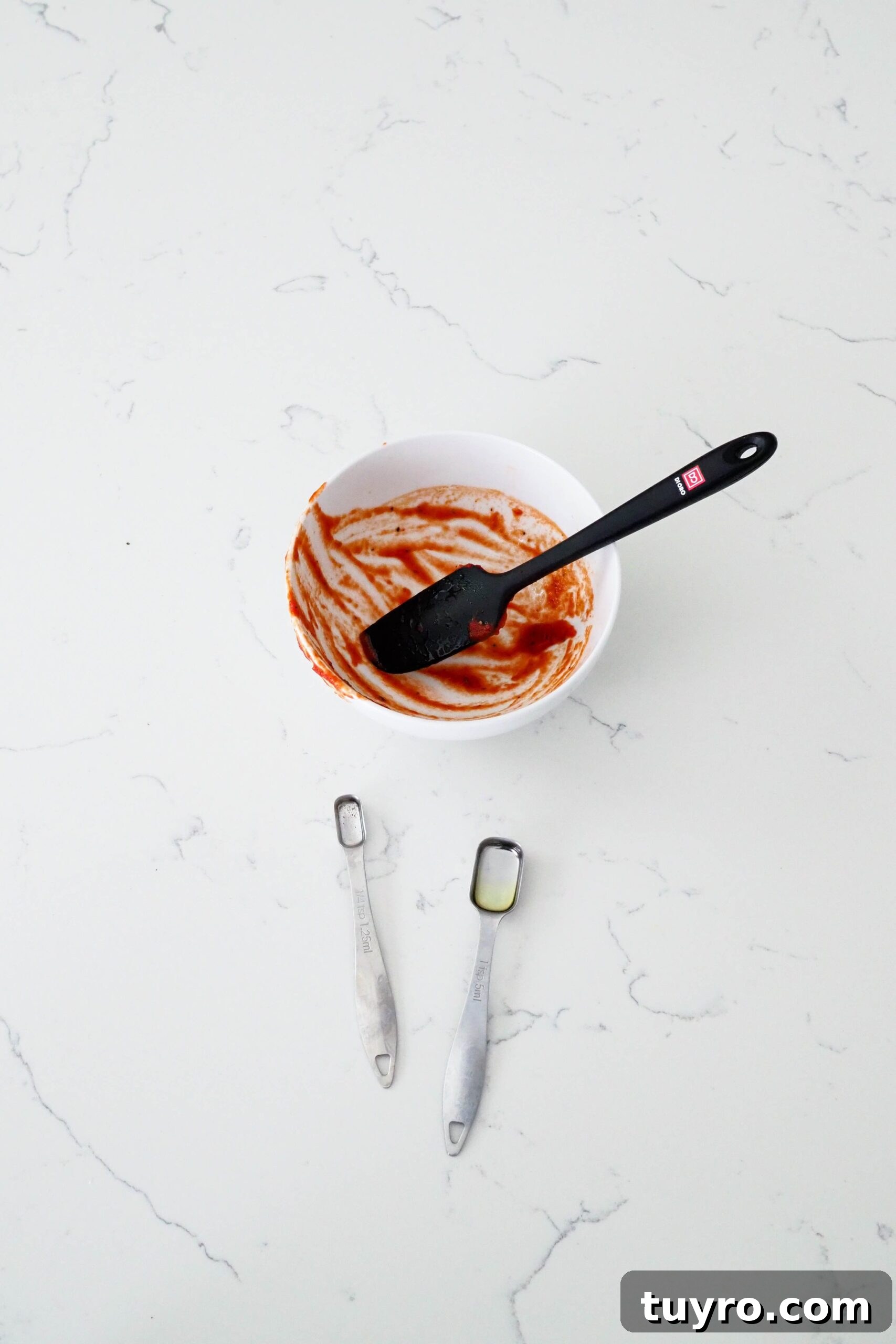 How to Make Pizza Sauce with Tomato Paste 7 A single bowl, spatula, and two measuring spoons on a quartz counter.