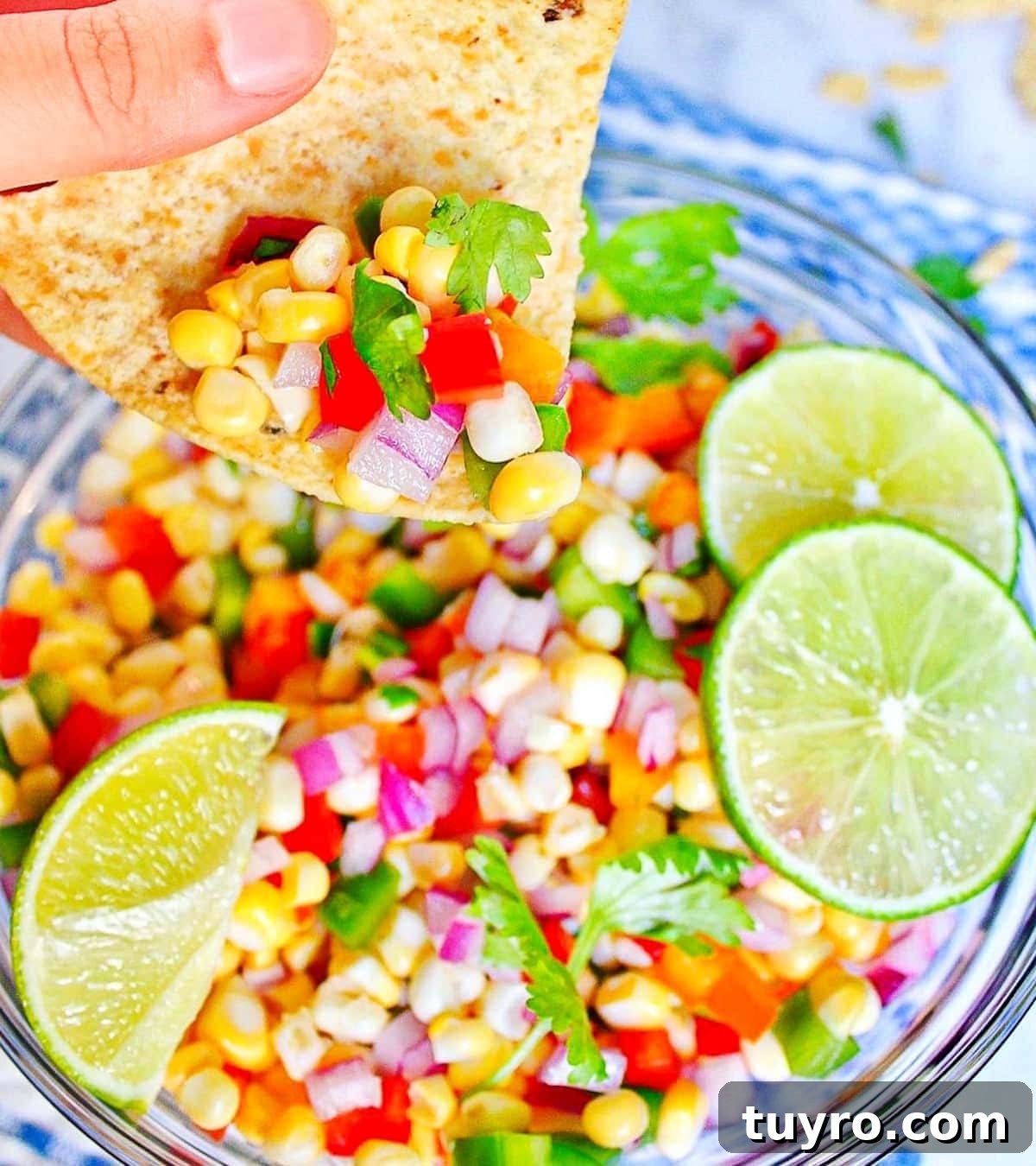 Fresh Corn Salsa Recipe: Zesty Vegan Side for Tacos & Chips 2 A hand holding a tortilla chip that is scooping corn salsa out of a round bowl.