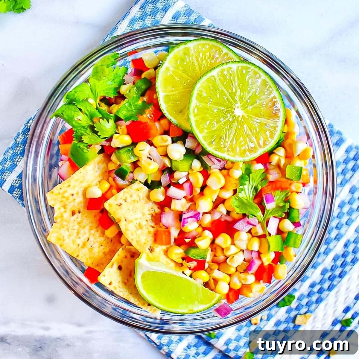 Fresh Corn Salsa Recipe: Zesty Vegan Side for Tacos & Chips 3 Picture of corn salsa in a round, glass bowl, garnished with sliced limes, cilantro, and tortilla chips.