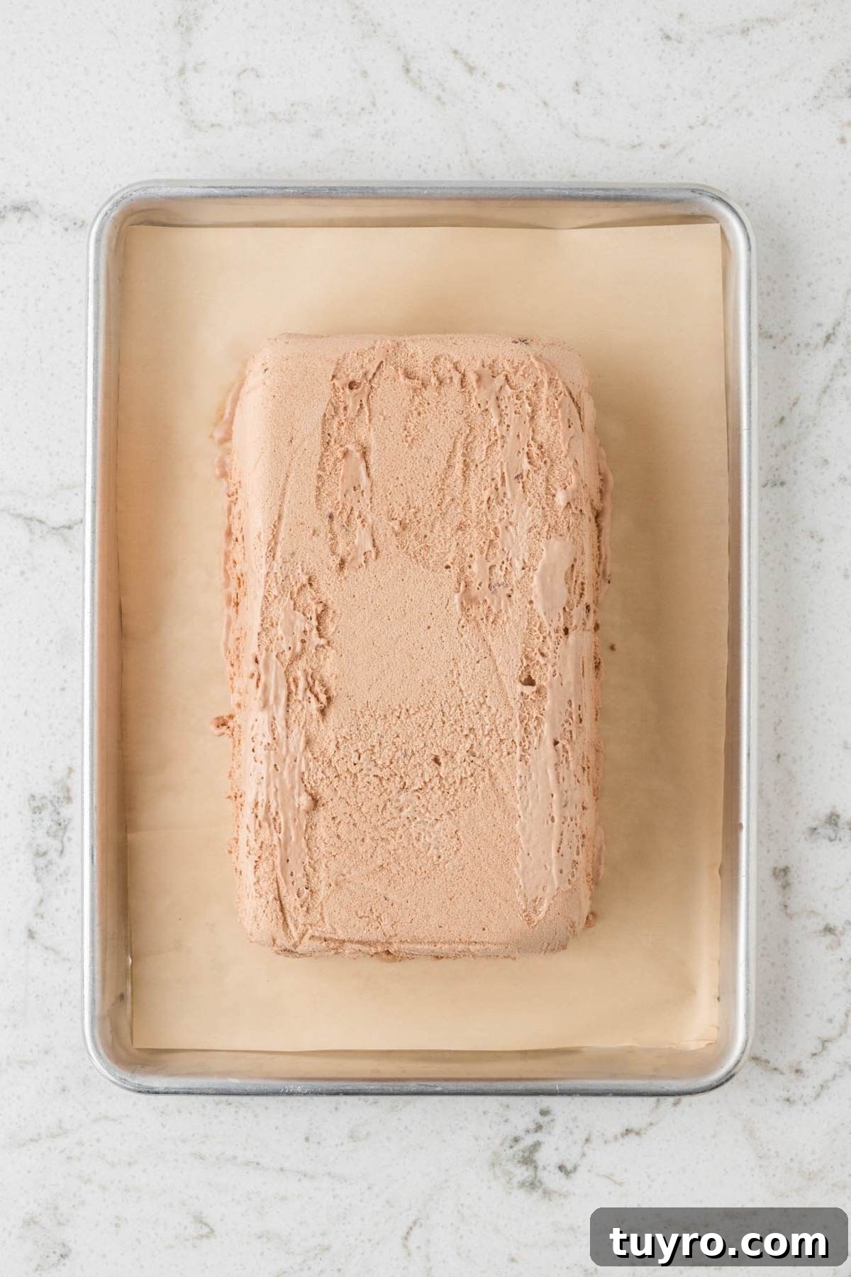 A rectangular loaf of chocolate ice cream on parchment paper in a metal baking tray.