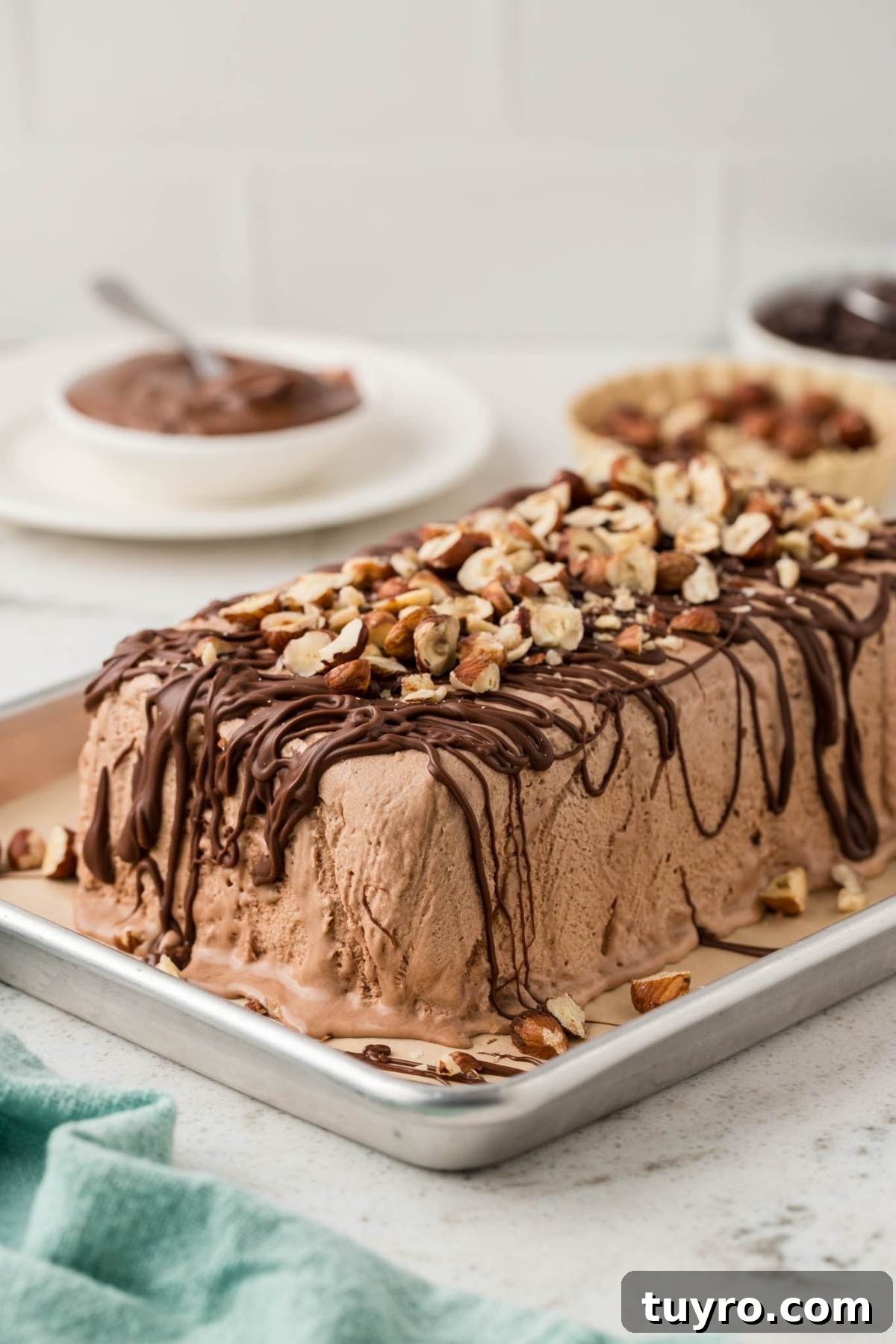 Rectangular chocolate ice cream dessert topped with chopped nuts and drizzled chocolate on a metal tray.