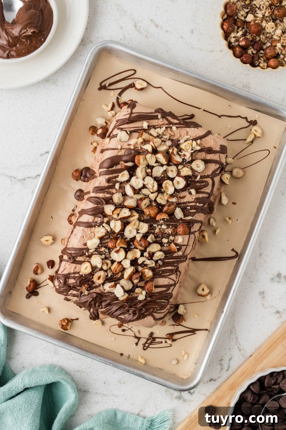 Chocolate ice cream loaf topped with drizzled chocolate and chopped hazelnuts on a parchment-lined baking sheet.