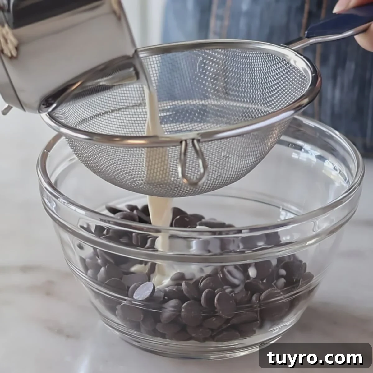 pouring cream through sieve over chocolate in glass bowl.