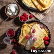 Danish Pandekager: Crispy-Edged Pancakes Recipe 6 Pandekager folded in triangles in a black, round backing dish, served with raspberries, icing sugar, jam and cream.