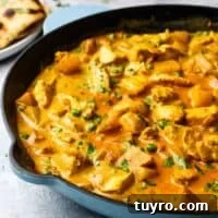 Chicken and Potato Curry Recipe 19 A cast iron pan full of chicken and potato curry garnished with cilantro, with a plate of naan bread in the background.